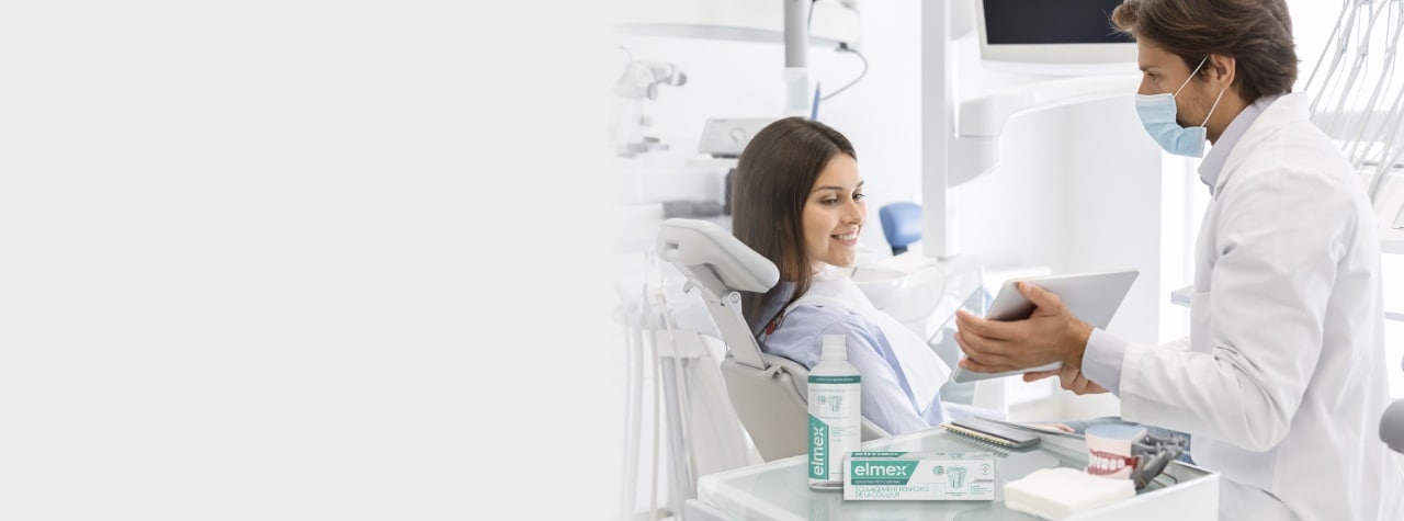 Un professionnel des soins dentaires portant un équipement EPI de sécurité et une blouse blanche souriant avec compassion